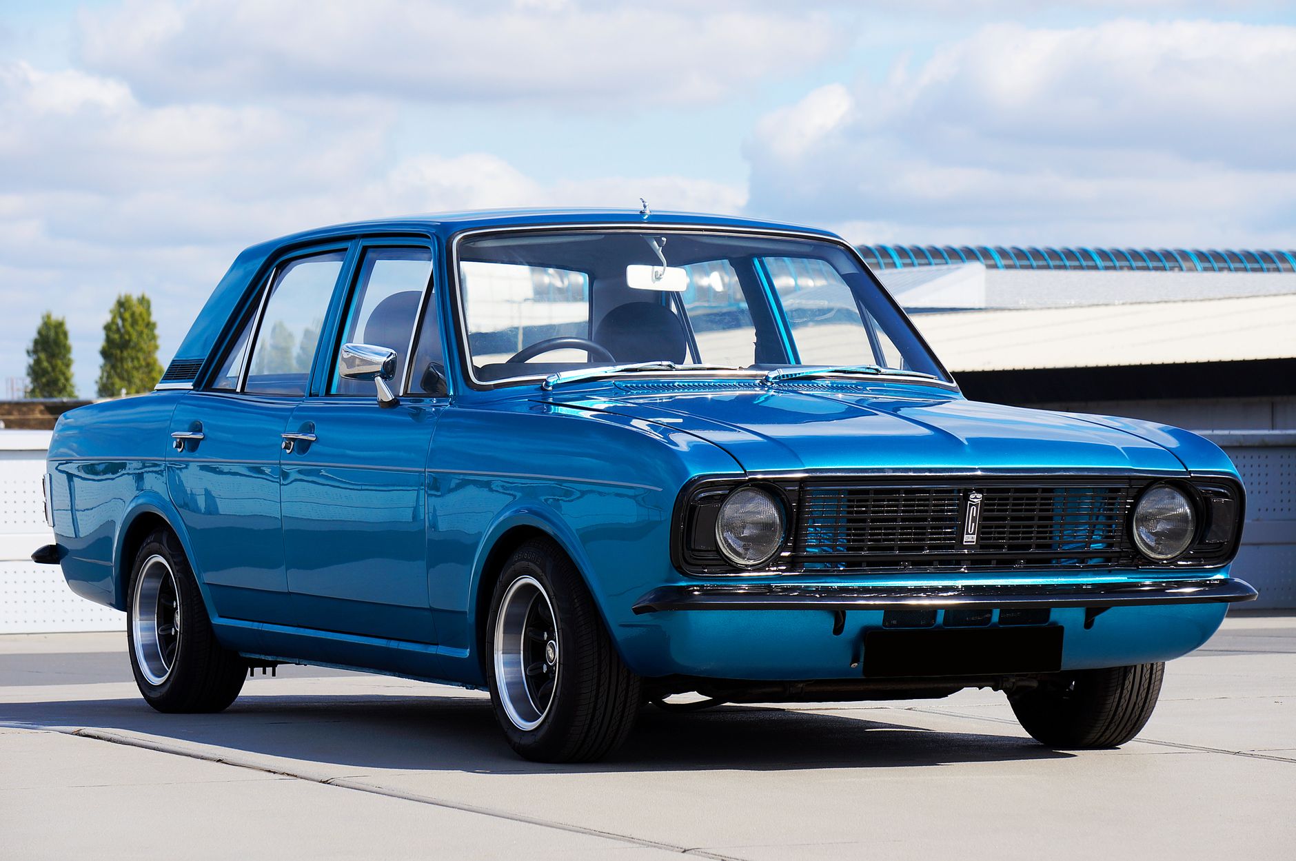 A beautifully restored vintage blue Ford Cortina parked outdoors on a sunny day, showcasing classic design.