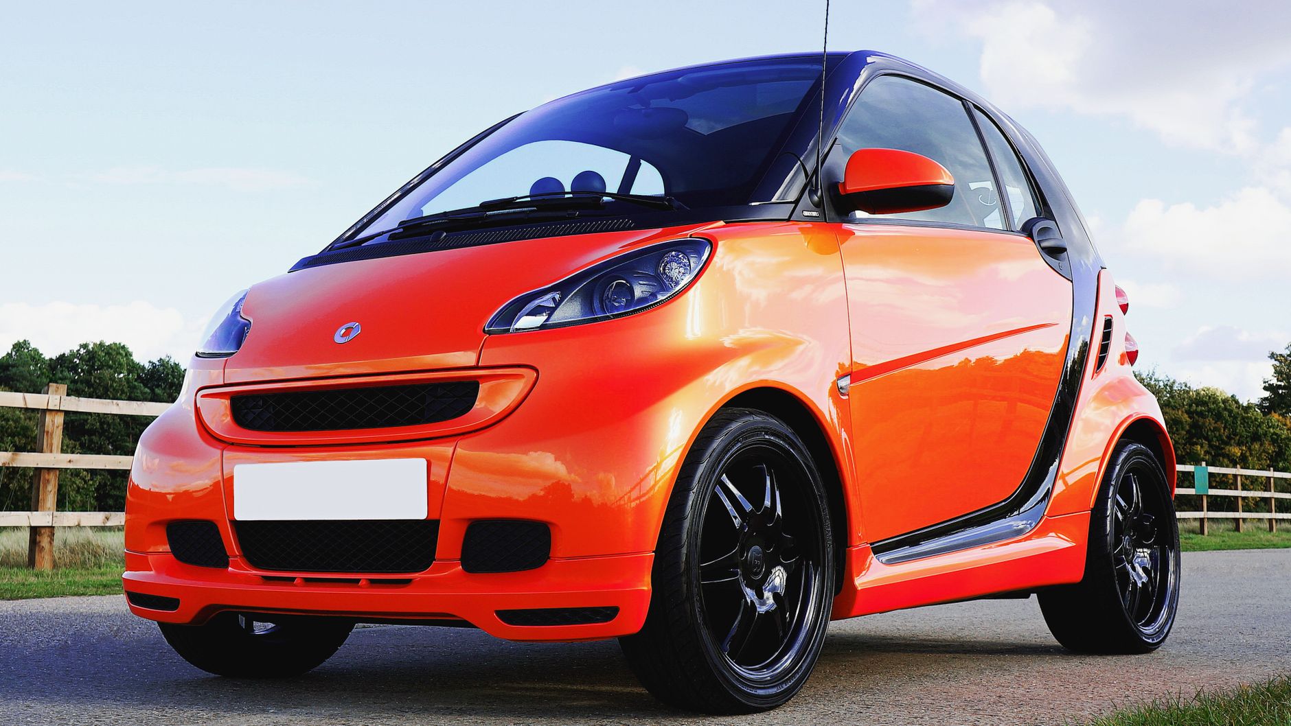 A vibrant orange microcar parked outdoors in Knebworth, England, under clear skies.