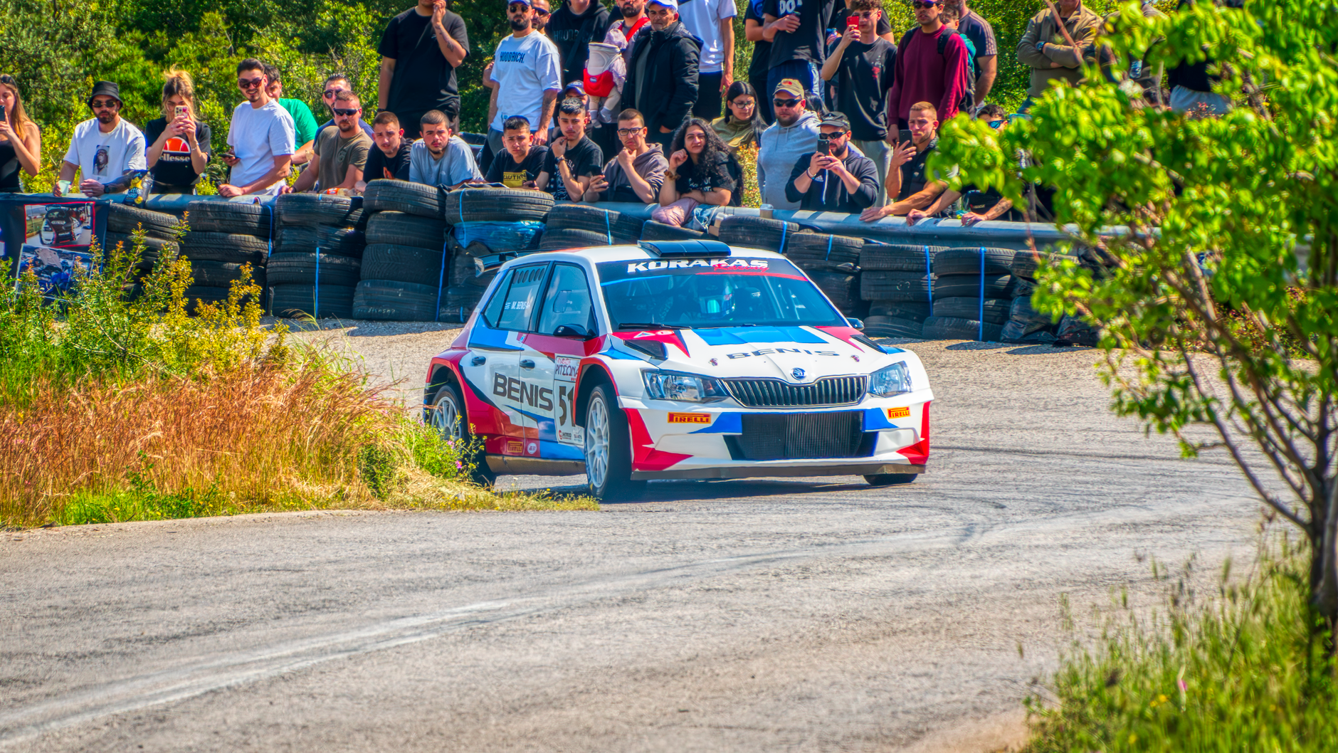 Rally car navigates a tight corner at a thrilling race event in Ritsona, Greece, surrounded by a crowd.