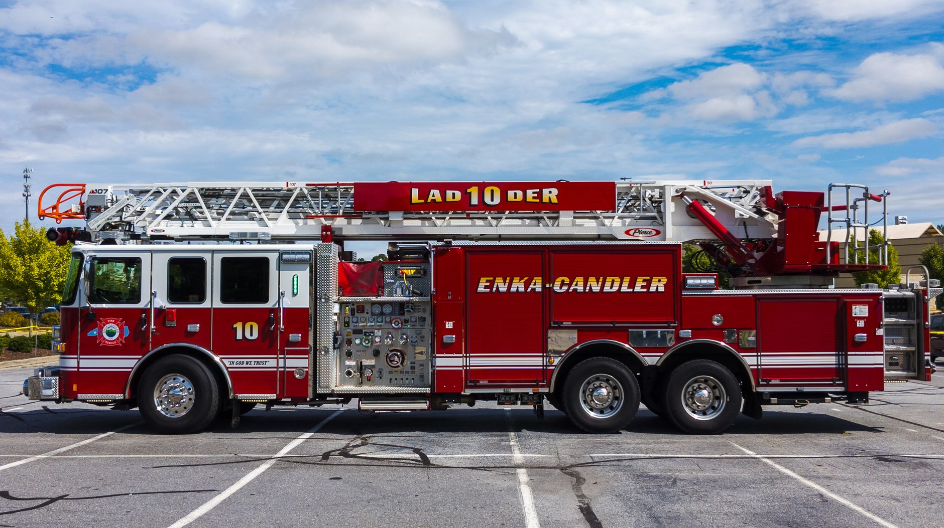 Side view of a red fire truck in an outdoor parking lot under a bright sky.