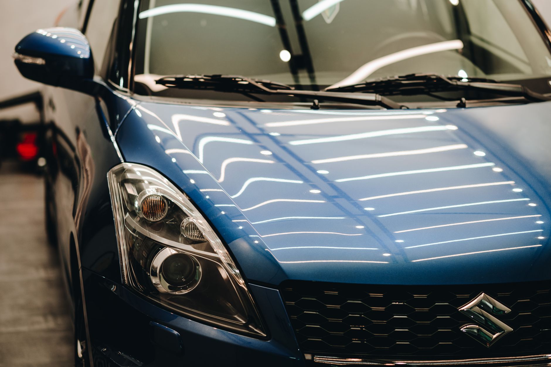 Close-up of a stylish blue Suzuki car displayed in a well-lit showroom with modern reflections.