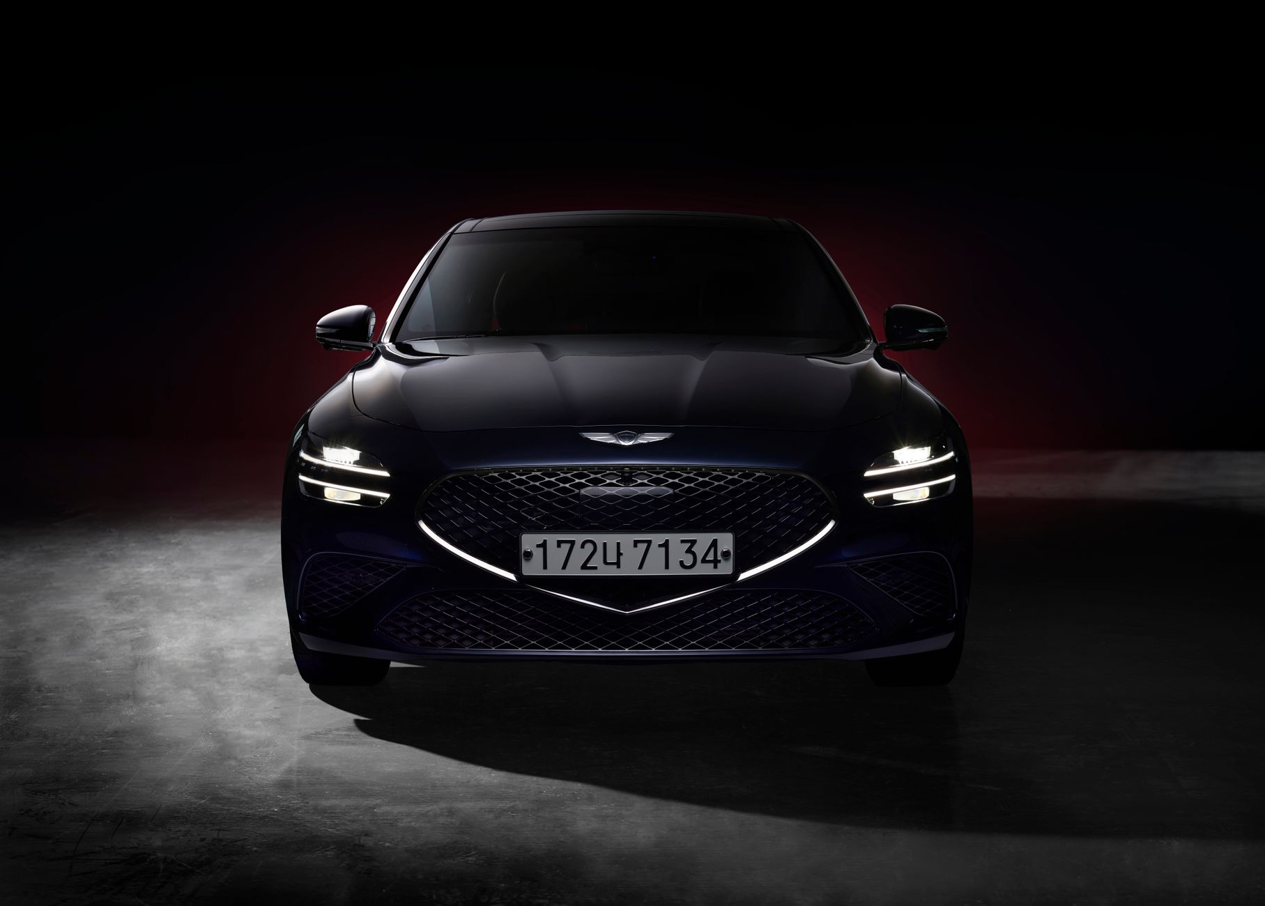 Front view of a sleek navy blue luxury sedan with distinctive headlights in a dramatic lighting setting.