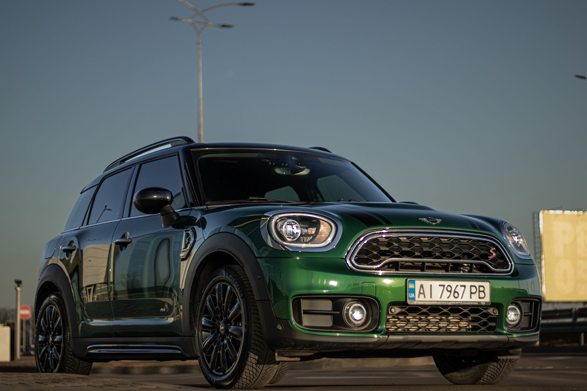 Green Mini Cooper SUV parked outdoors with headlights on, featuring a shiny exterior.