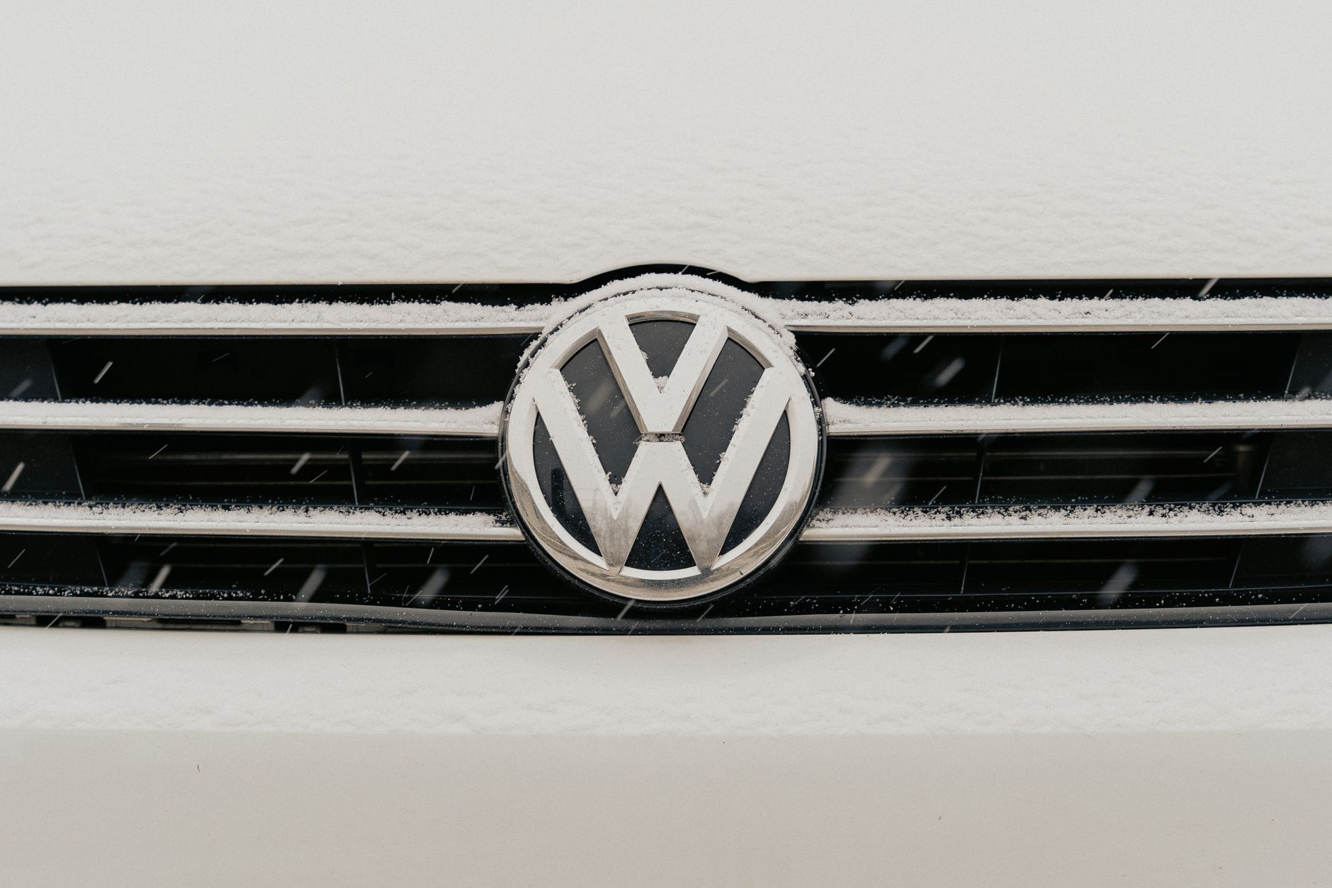 Closeup of a snow-dusted Volkswagen car grille shows the iconic VW logo.