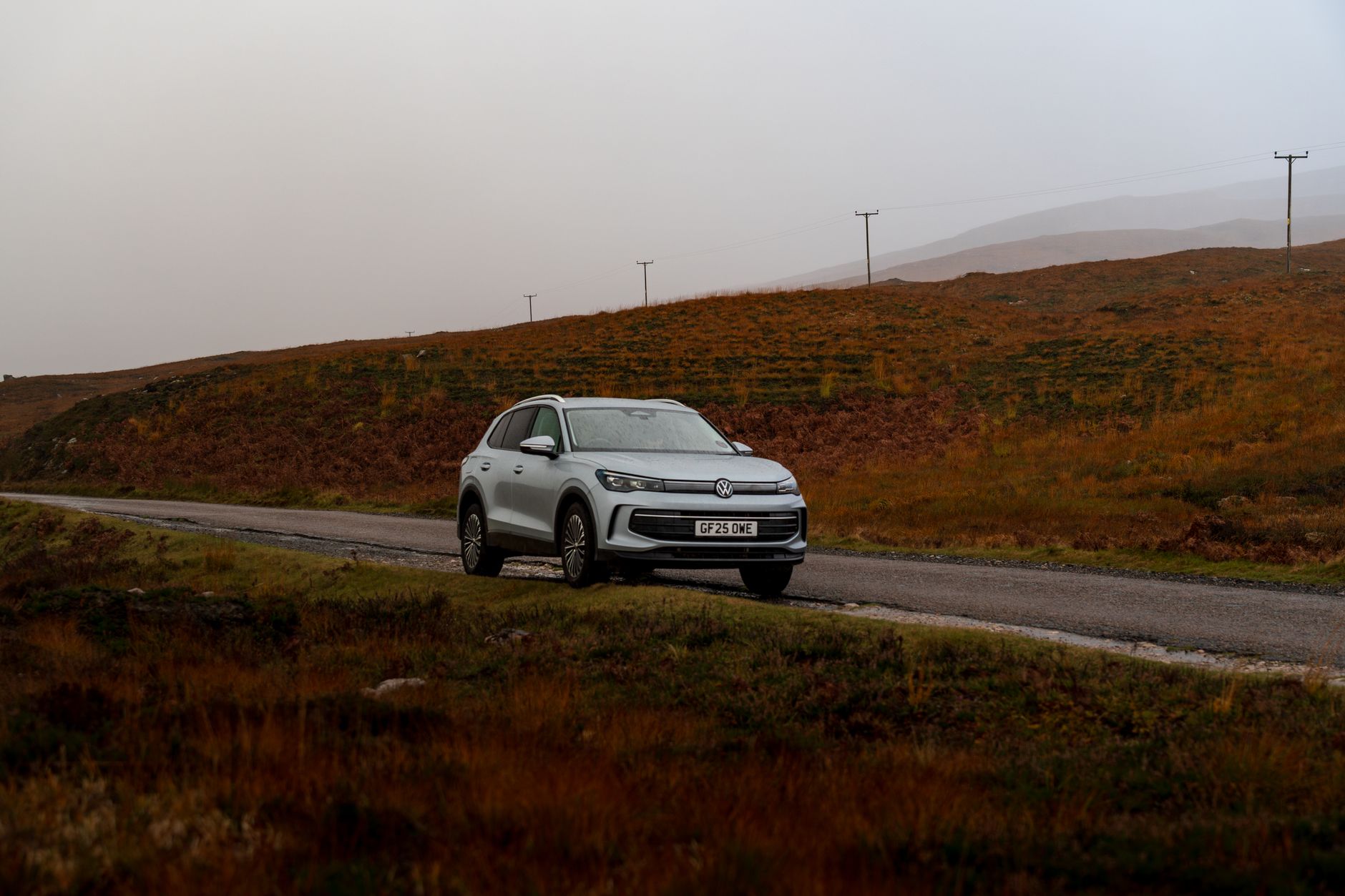 A silver SUV traveling on a scenic, remote road in the highlands during autumn.