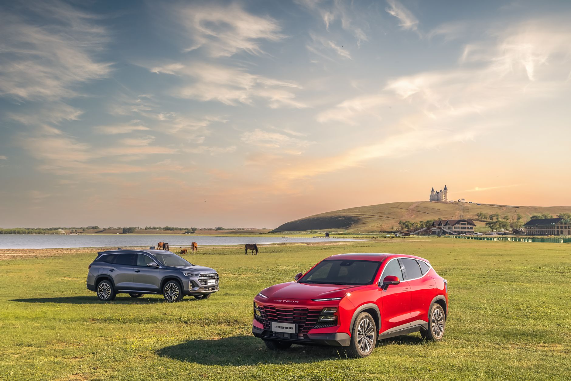 Two Jetour SUVs parked in a scenic Georgian landscape with a lake and horses, showcasing countryside elegance.