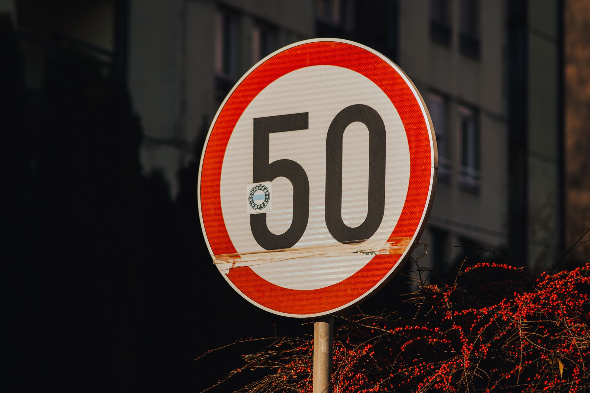 A close-up of a 50 km/h speed limit sign against a city backdrop.