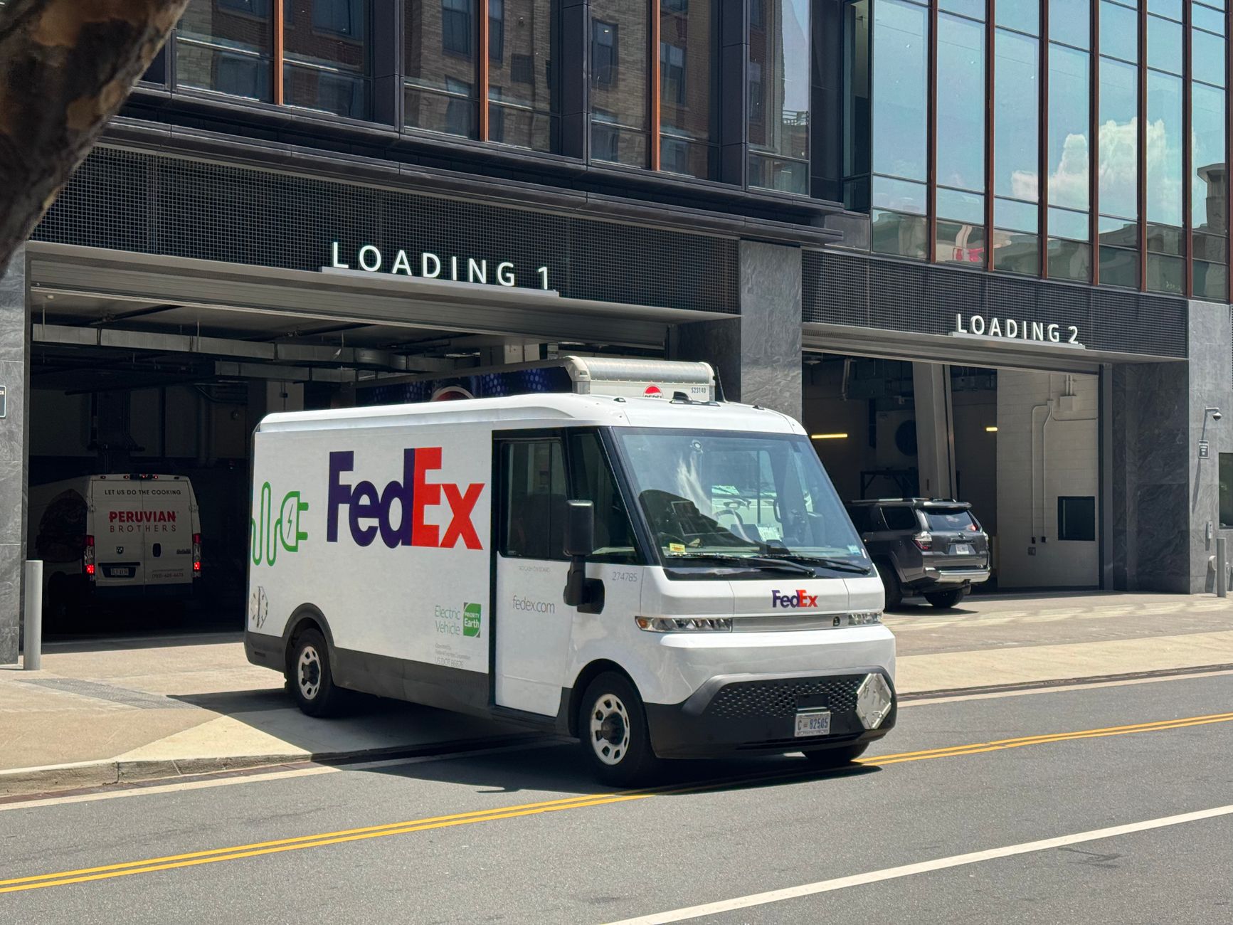 FedEx electric van parked outside a loading dock in a city environment, promoting green delivery.