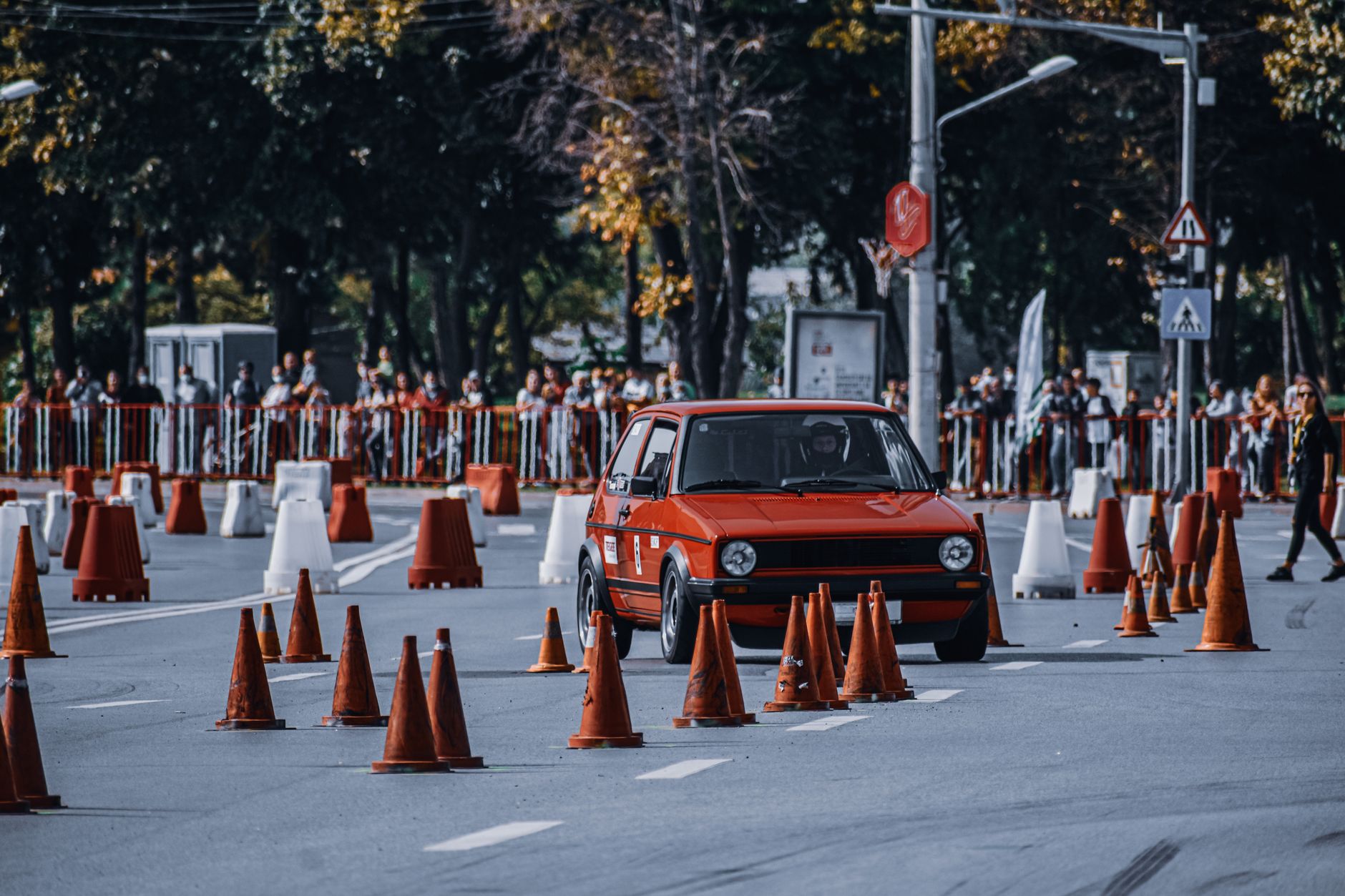 Unrecognizable person driving red spots car on asphalt road with orange road cones during competition in daytime