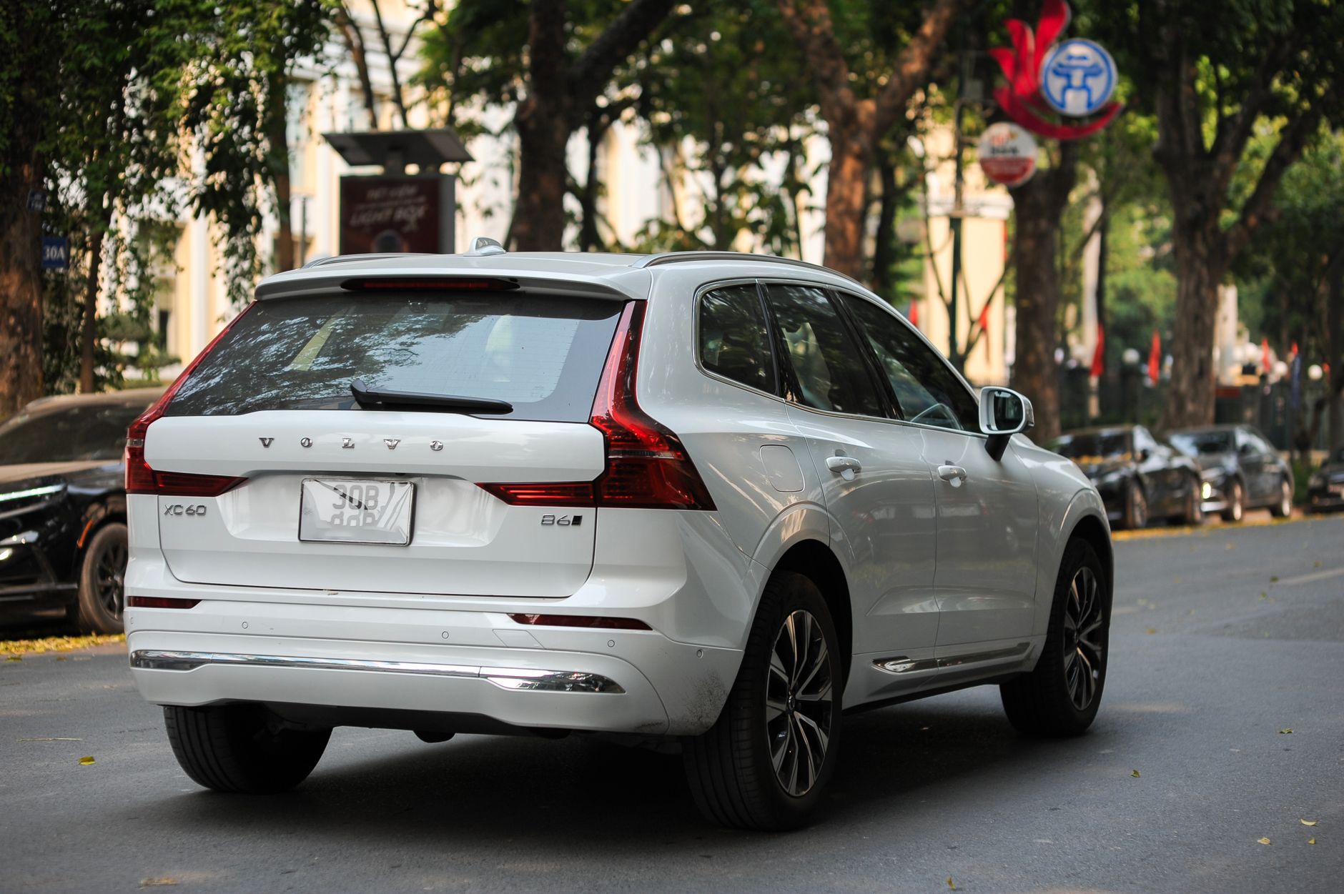 A white Volvo XC60 parked on a tree-lined street in a city setting.