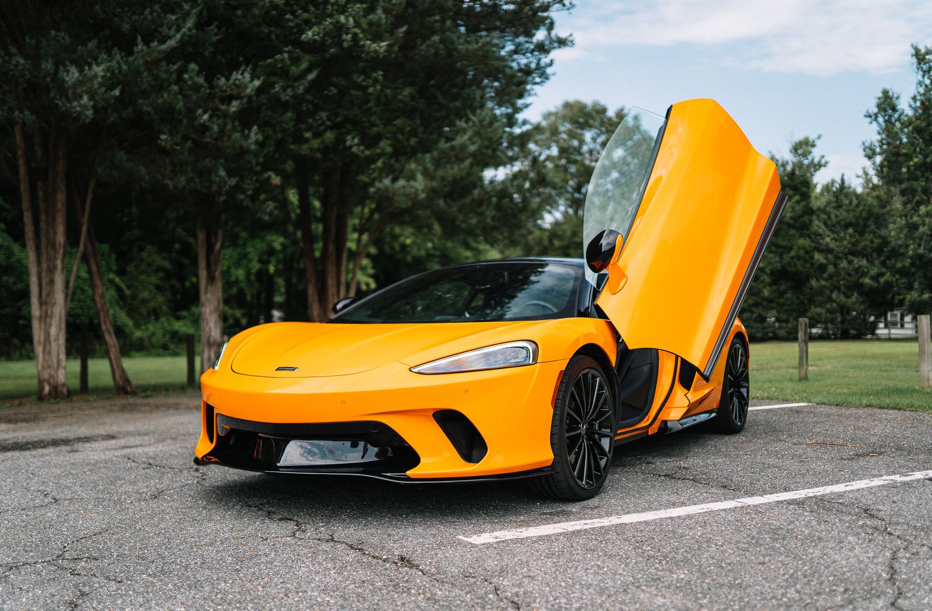 A sleek orange supercar with upward doors parked in a tranquil setting.