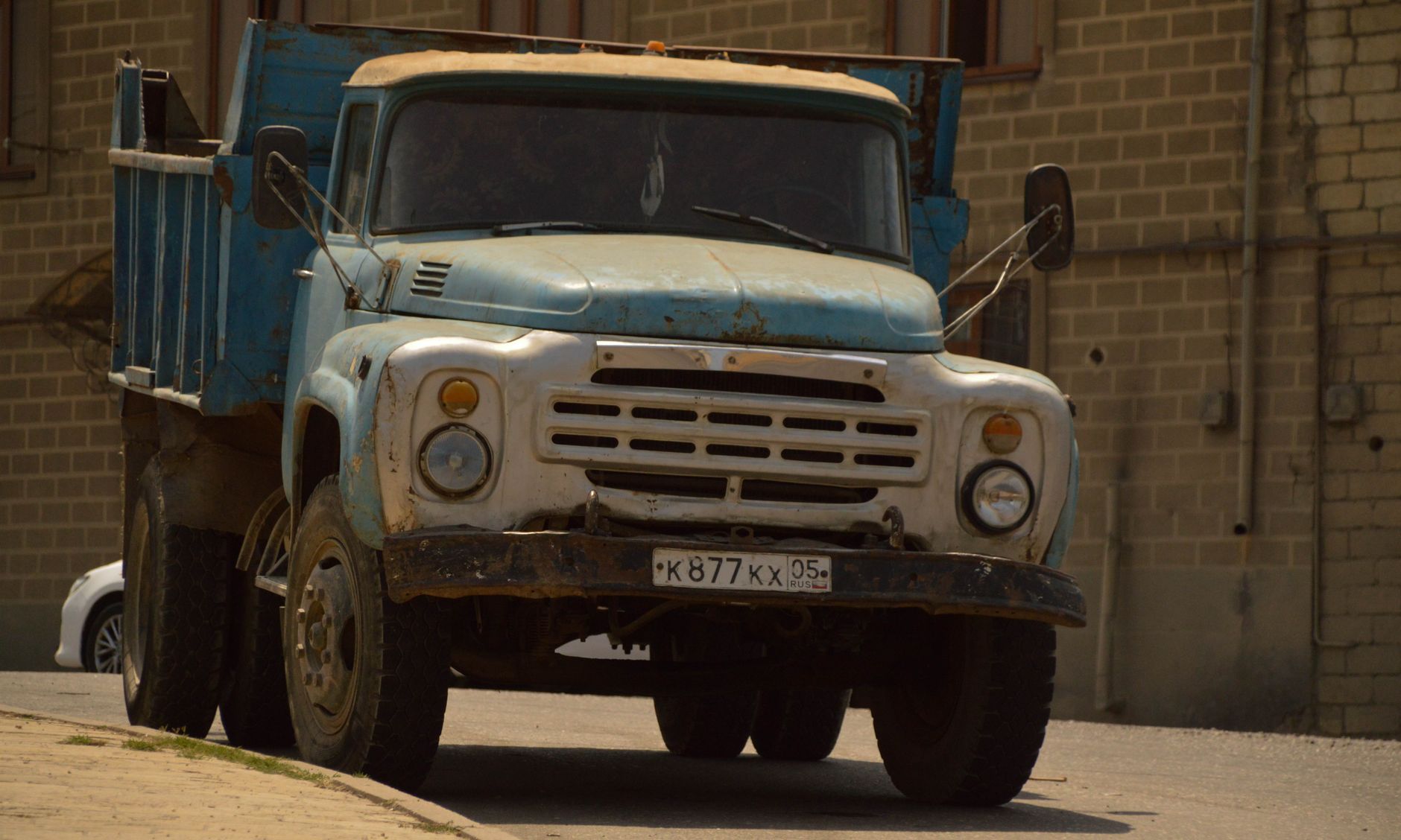 Rustic blue ZIL-130 truck parked on a city street with a brick building backdrop.