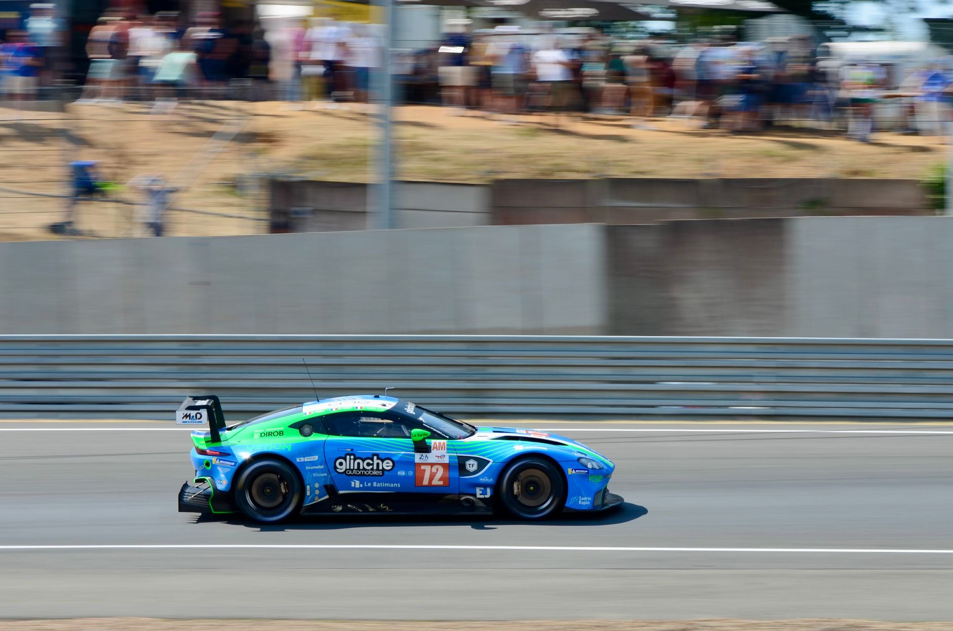 Aston Martin car racing at high speed on Le Mans Circuit in France, captured during a motorsport competition.