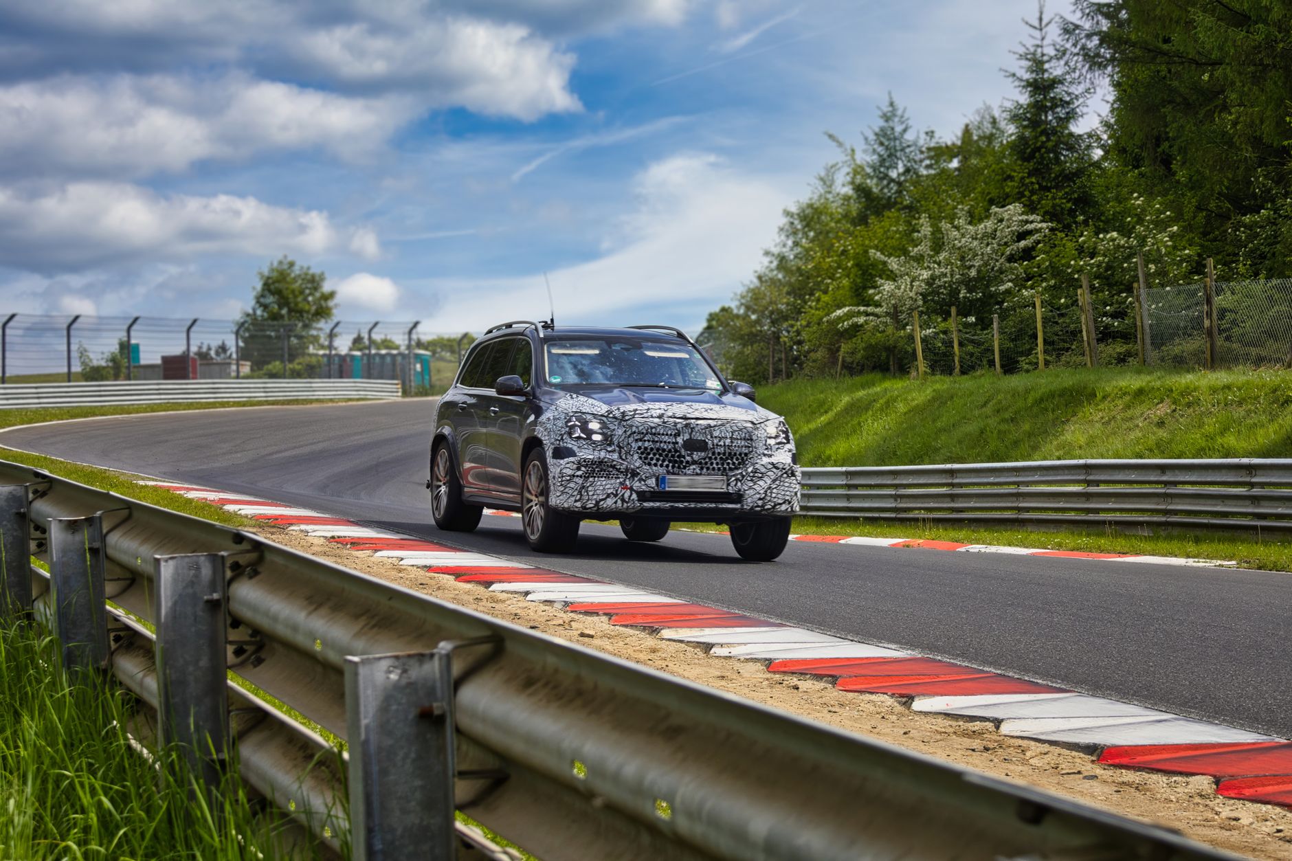 A camouflaged car navigates a curve on the iconic Nurburgring race track during a clear summer day.