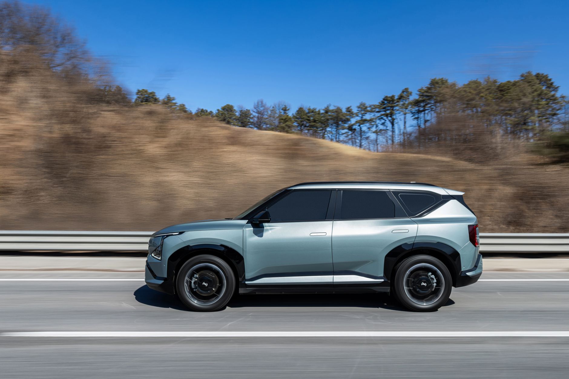 A stylish electric SUV driving on a highway with a clear blue sky and scenic background.