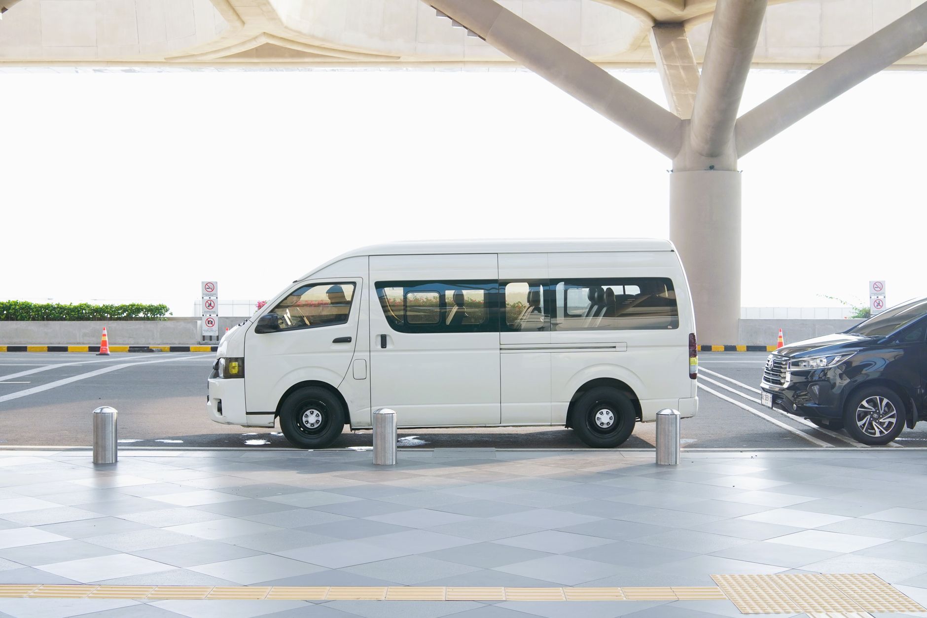 A white minivan parked at a modern airport terminal drop-off zone, ideal for travel and transport concepts.