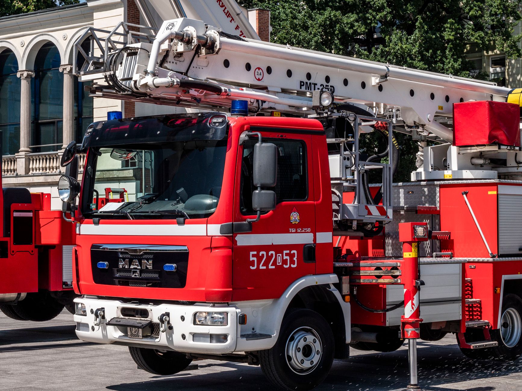 Red fire truck with aerial ladder parked in front of a historic building on a sunny day.