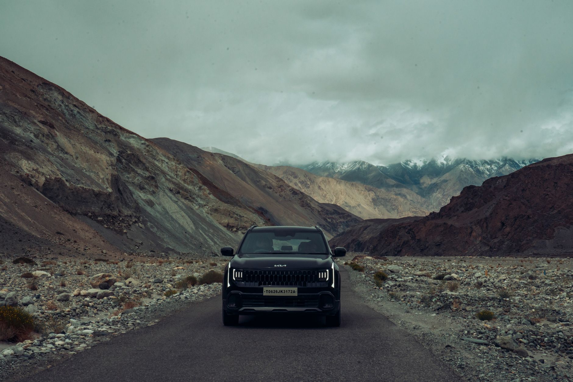 A black SUV navigating through the rugged, scenic mountain roads of Ladakh under an overcast sky.