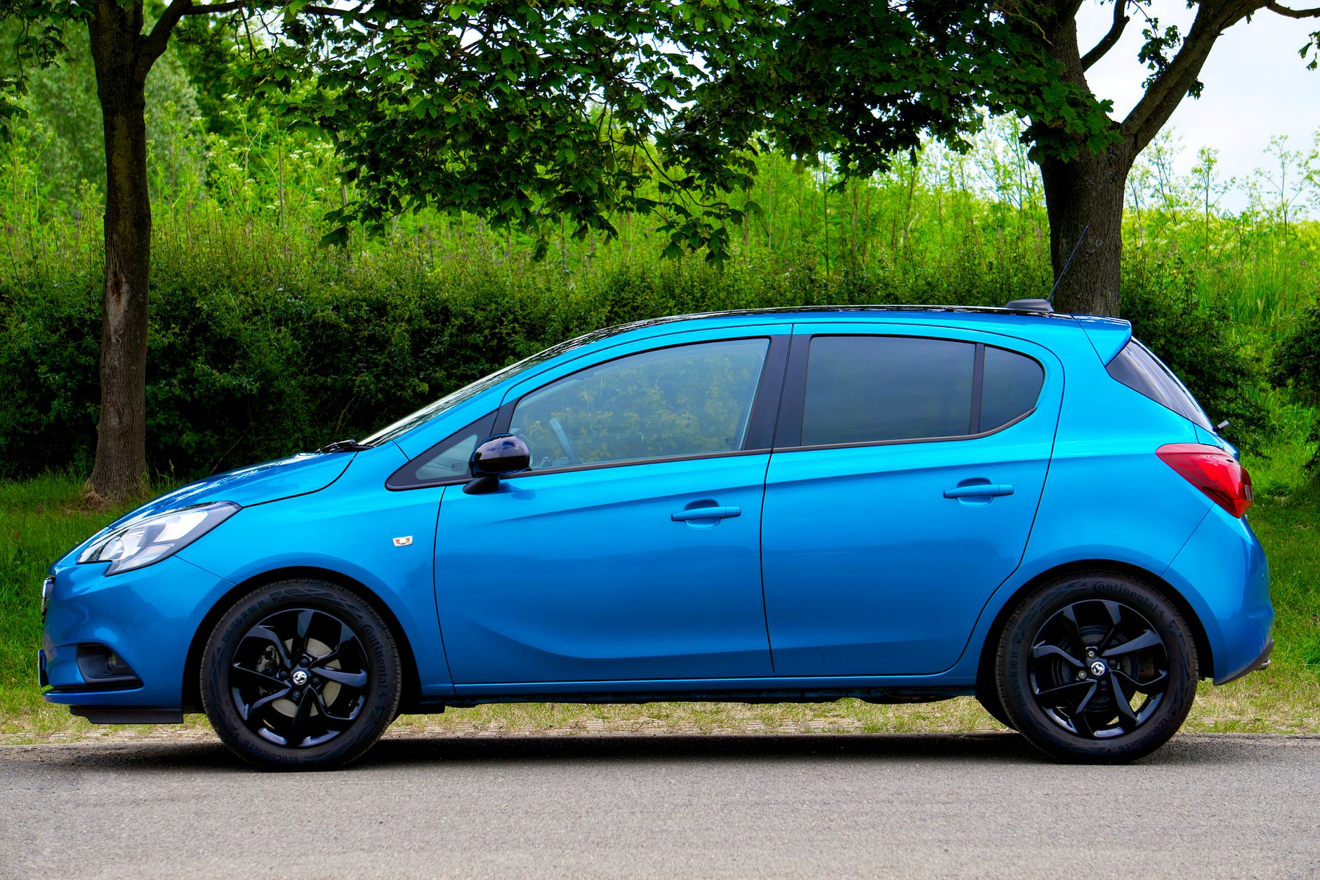 A sleek blue compact car parked on a scenic tree-lined road on a sunny day.