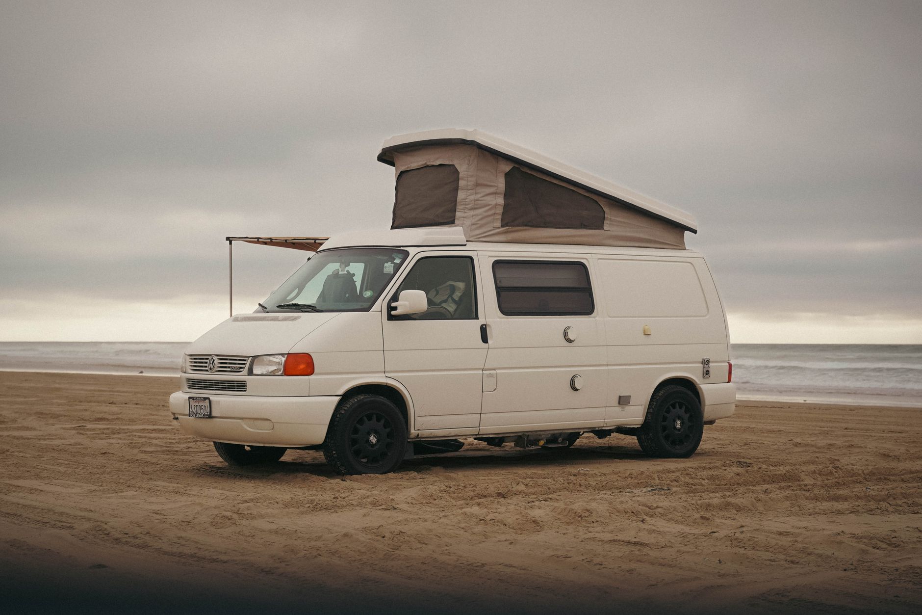 A classic Volkswagen camper van parked on the sandy shore of Oceano Beach, California.