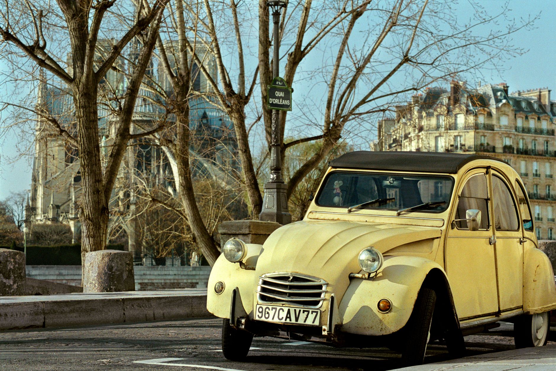 A classic Citroën 2CV car parked by Notre-Dame Cathedral in Paris.