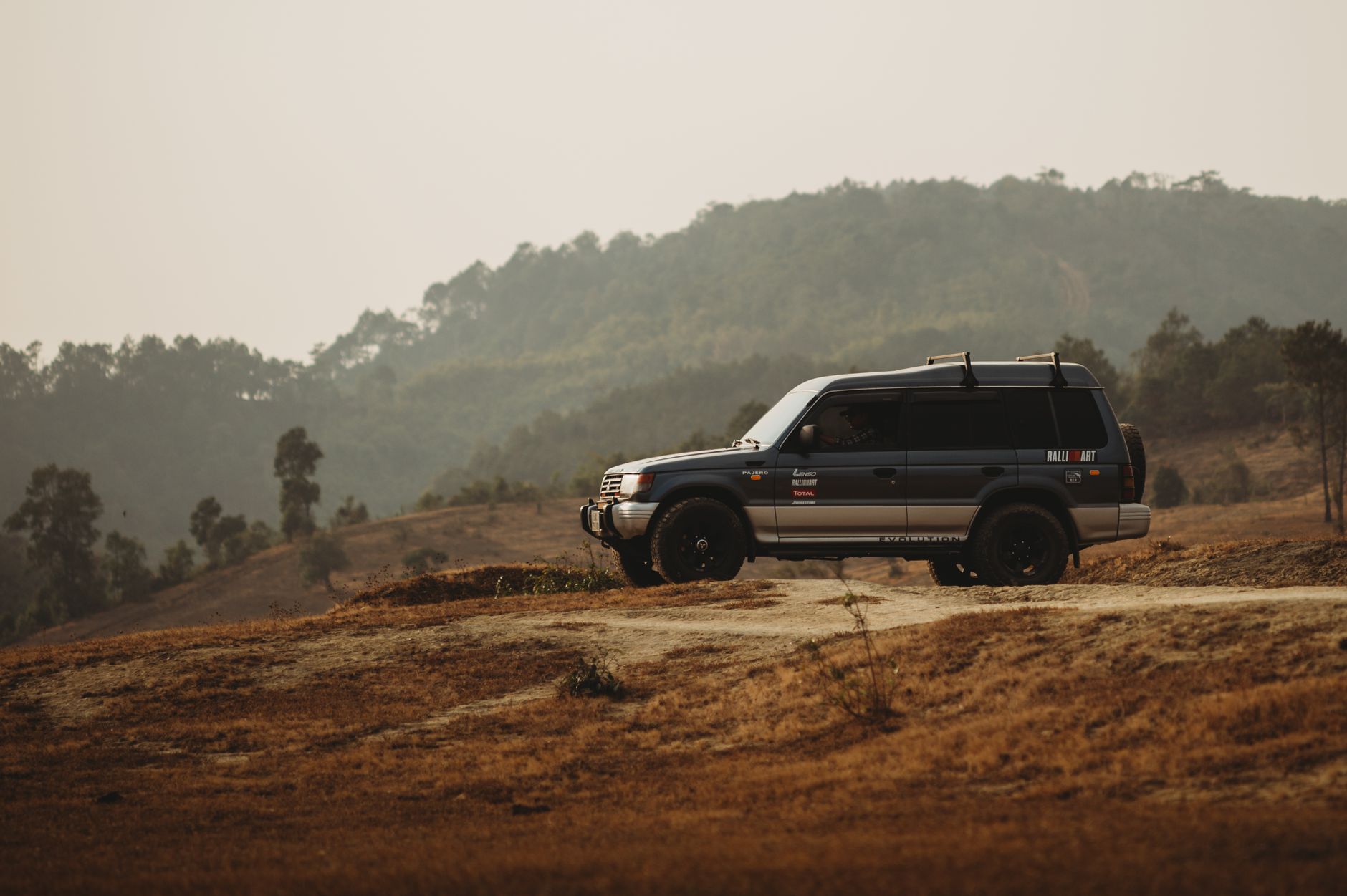 A Mitsubishi Pajero SUV navigating a dirt road surrounded by hills and trees. Perfect for adventure themes.