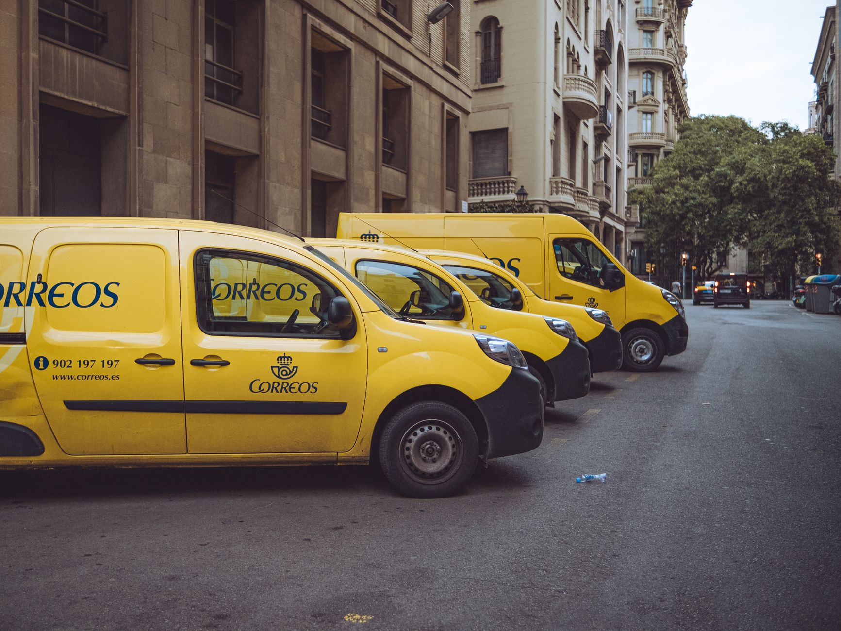 Three yellow delivery vans parked on a street in Barcelona, Spain, showcasing urban logistics.