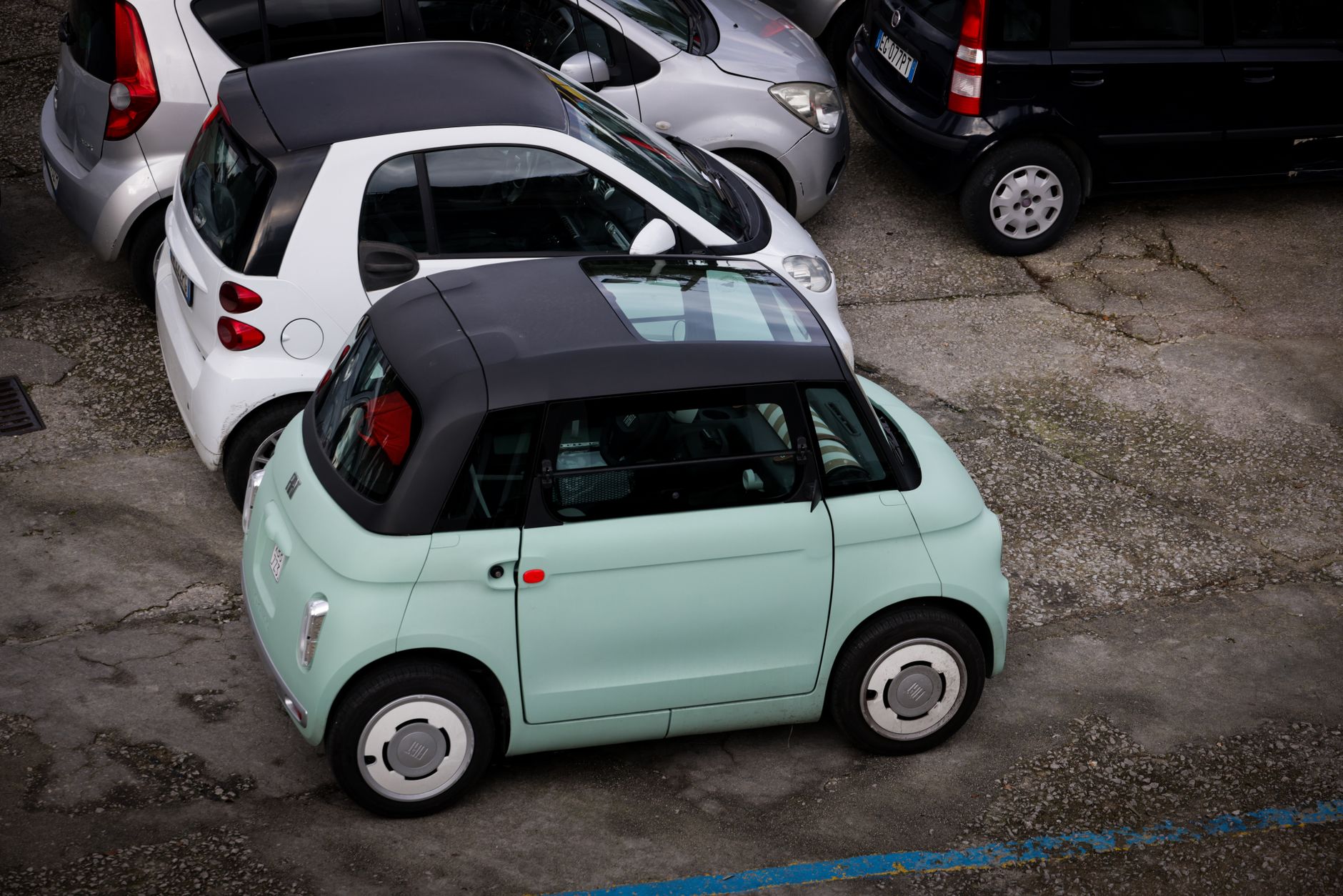 A selection of compact cars parked closely in an outdoor urban parking lot.