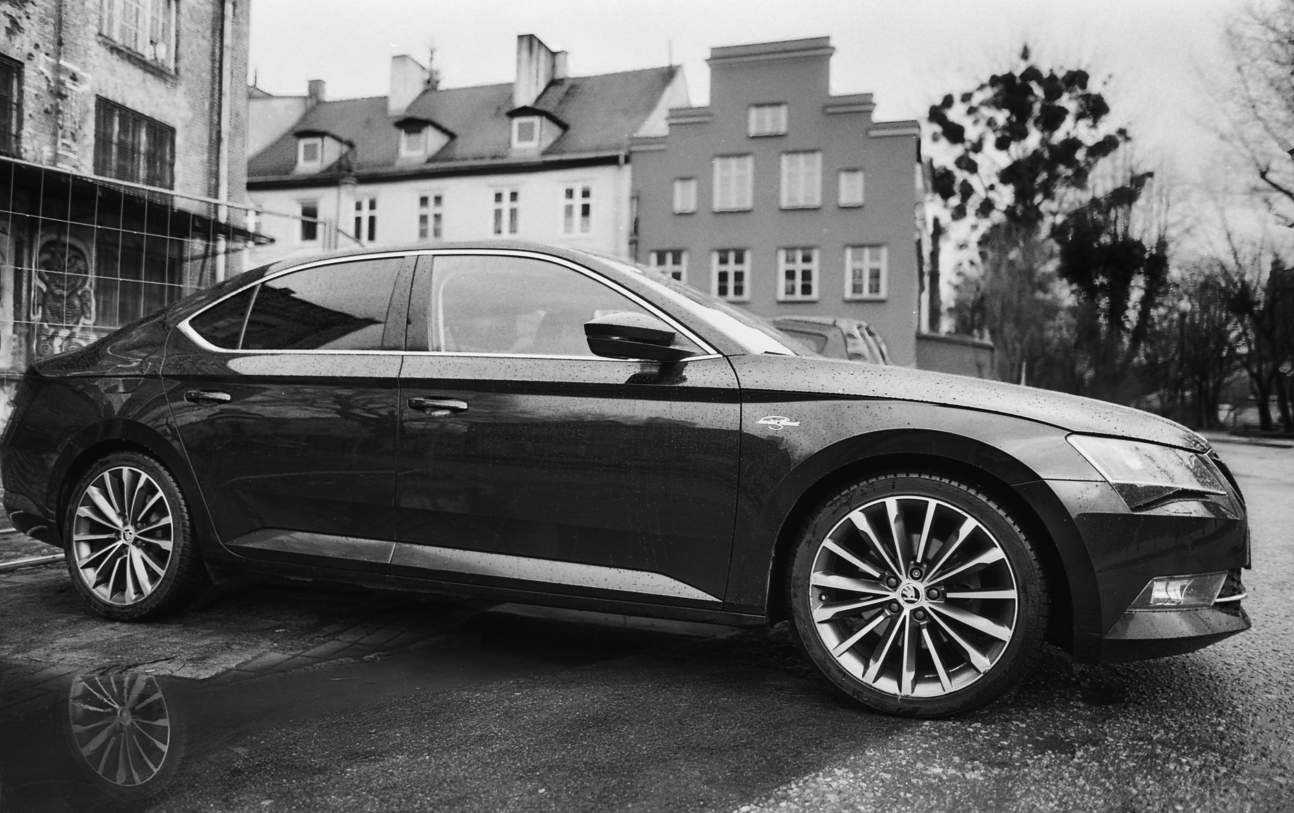 Black and white photo of a Skoda car parked on a city street with buildings in the background.