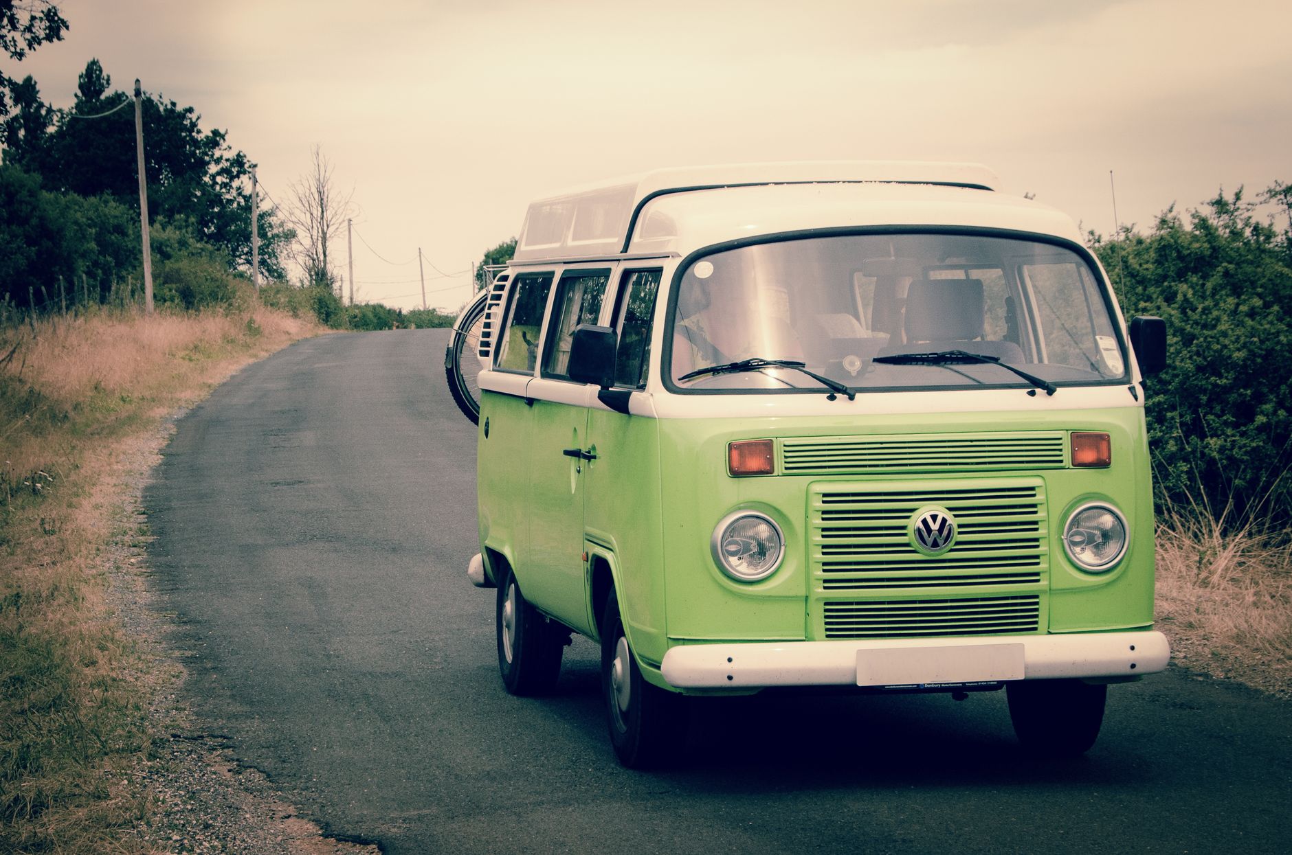 Classic green Volkswagen campervan driving on a quiet country road, perfect for road trips and adventure in nature.