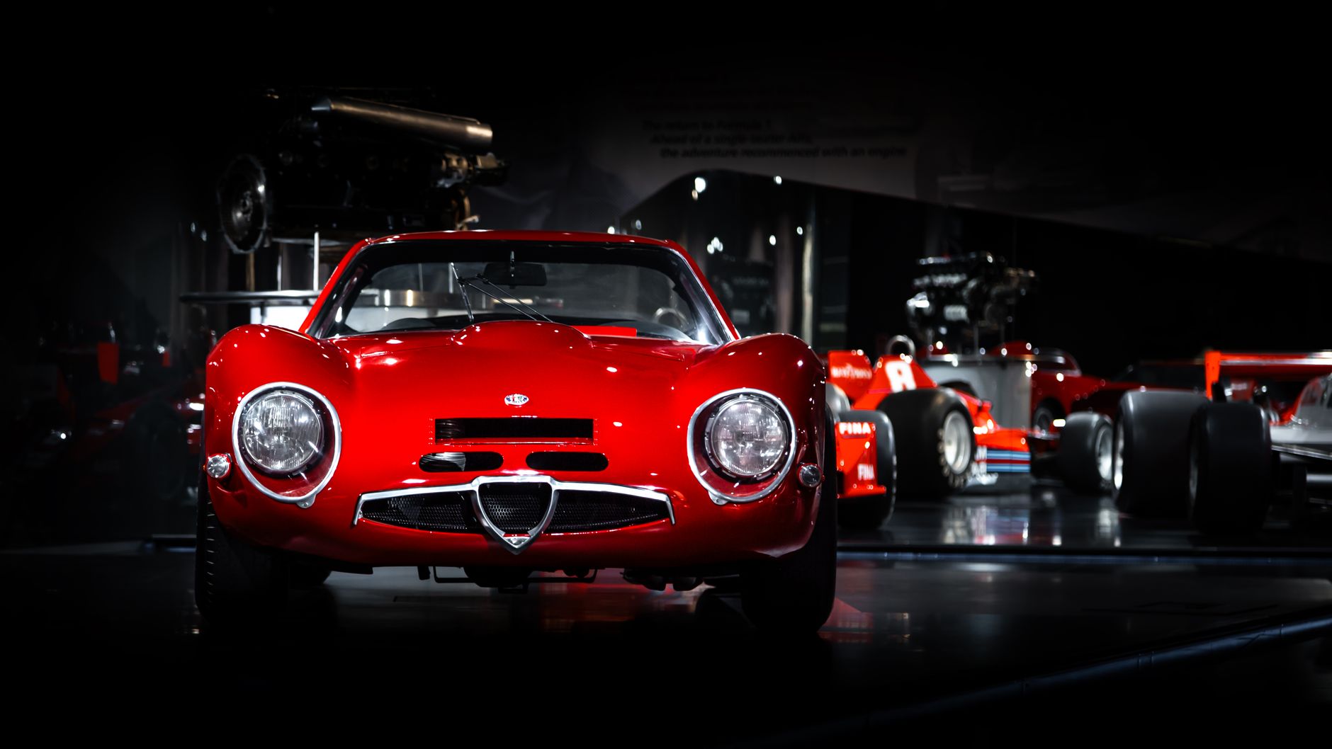 Iconic red Alfa Romeo sports car displayed in a dimly lit museum setting.