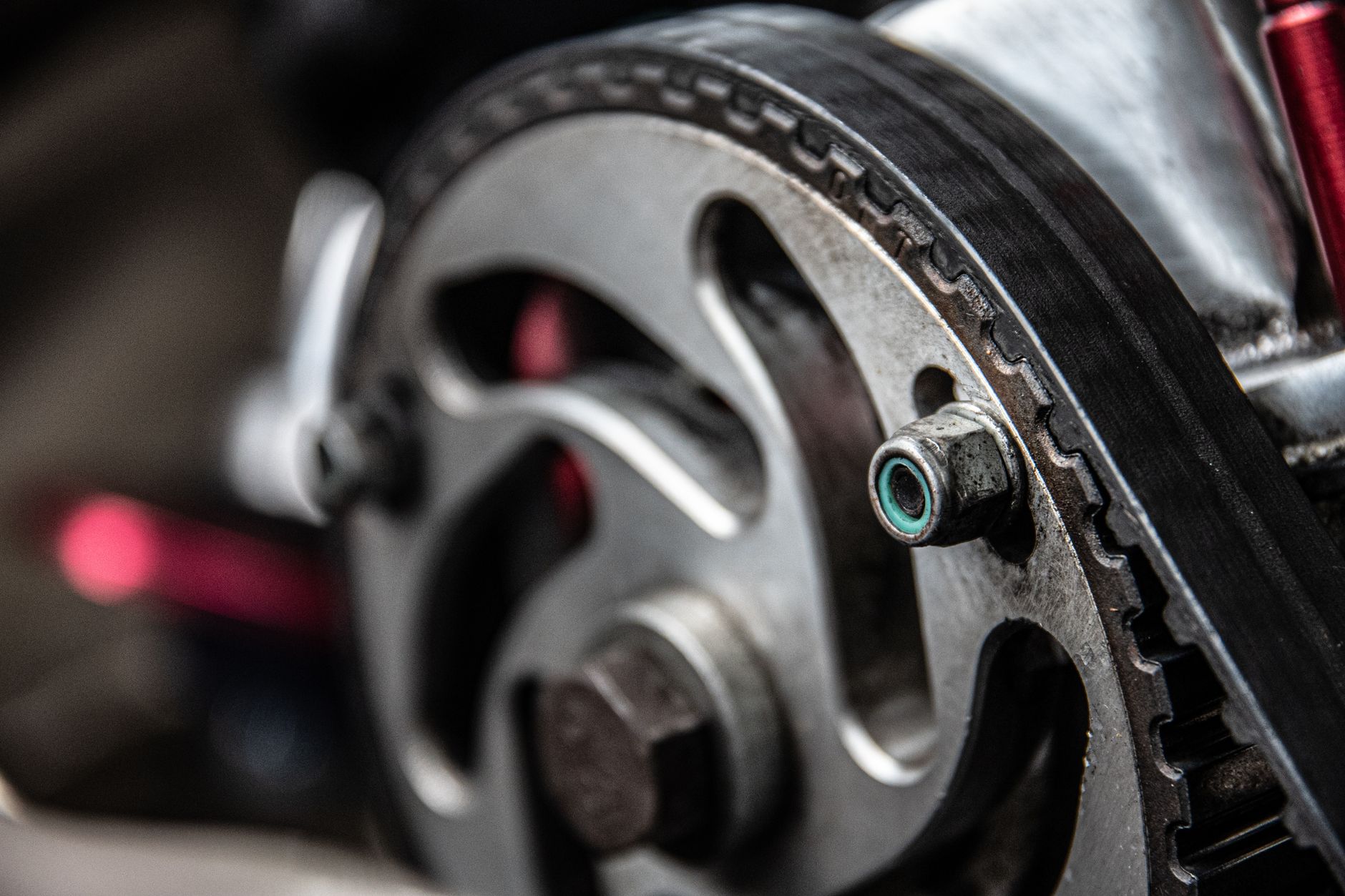 Closeup of black thin timing belt on round metallic camshaft sprocket in daylight on blurred background