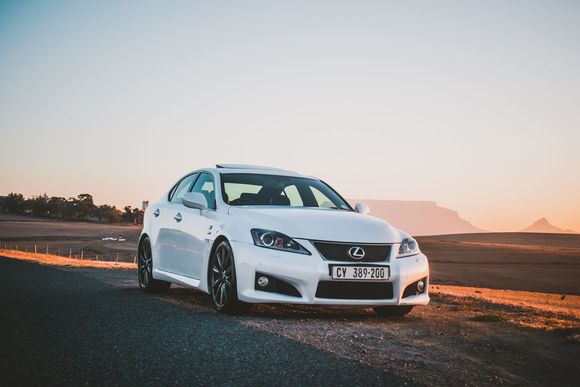 A white Lexus sedan parked by a scenic road during a stunning sunset, showcasing beauty and elegance.