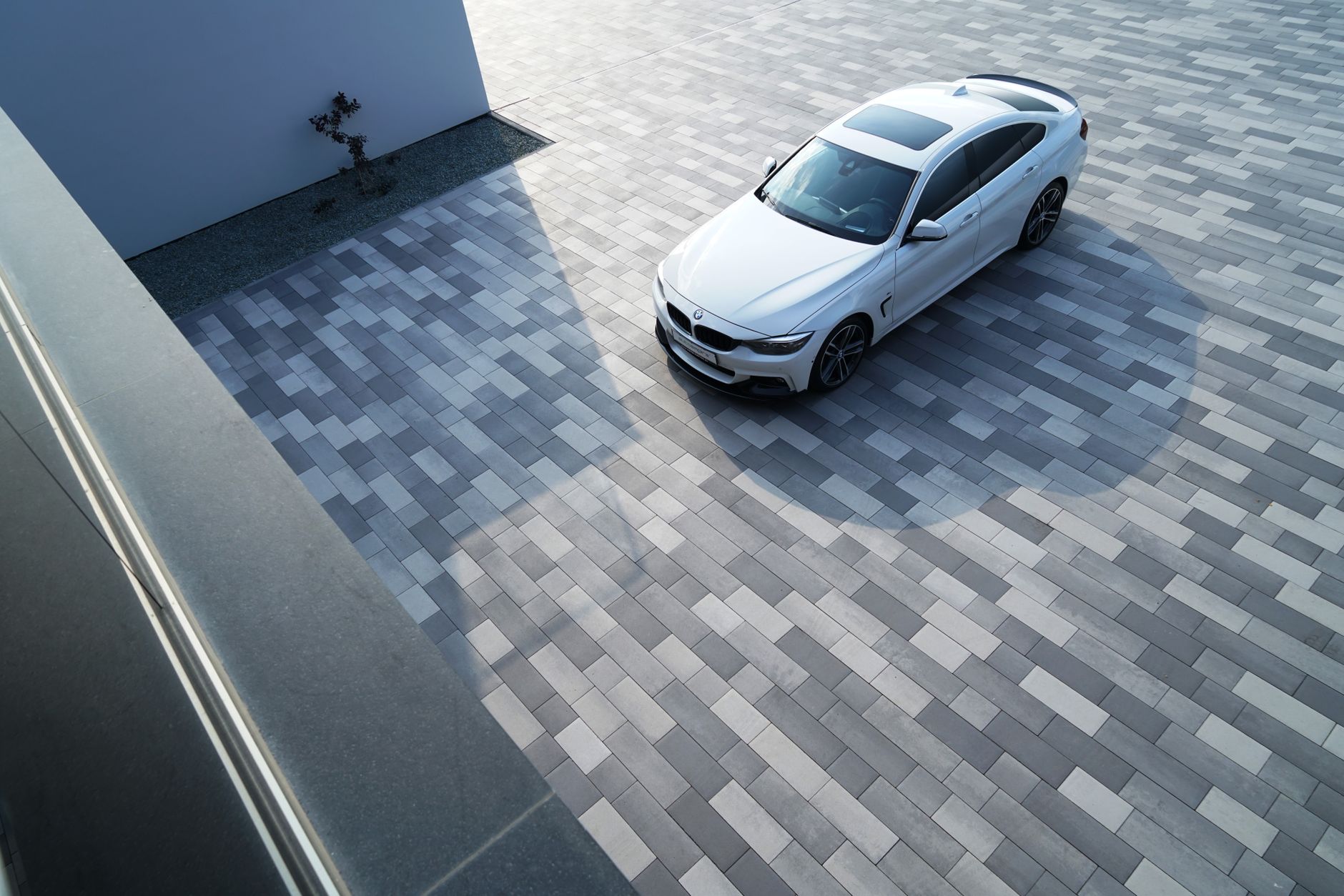 A white BMW 3 Series parked on contemporary geometric pavement, showcasing modern urban design.