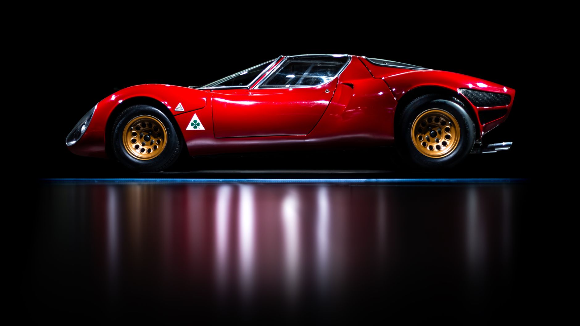 A striking red classic sports car with a sleek side profile, reflecting elegance and vintage charm.