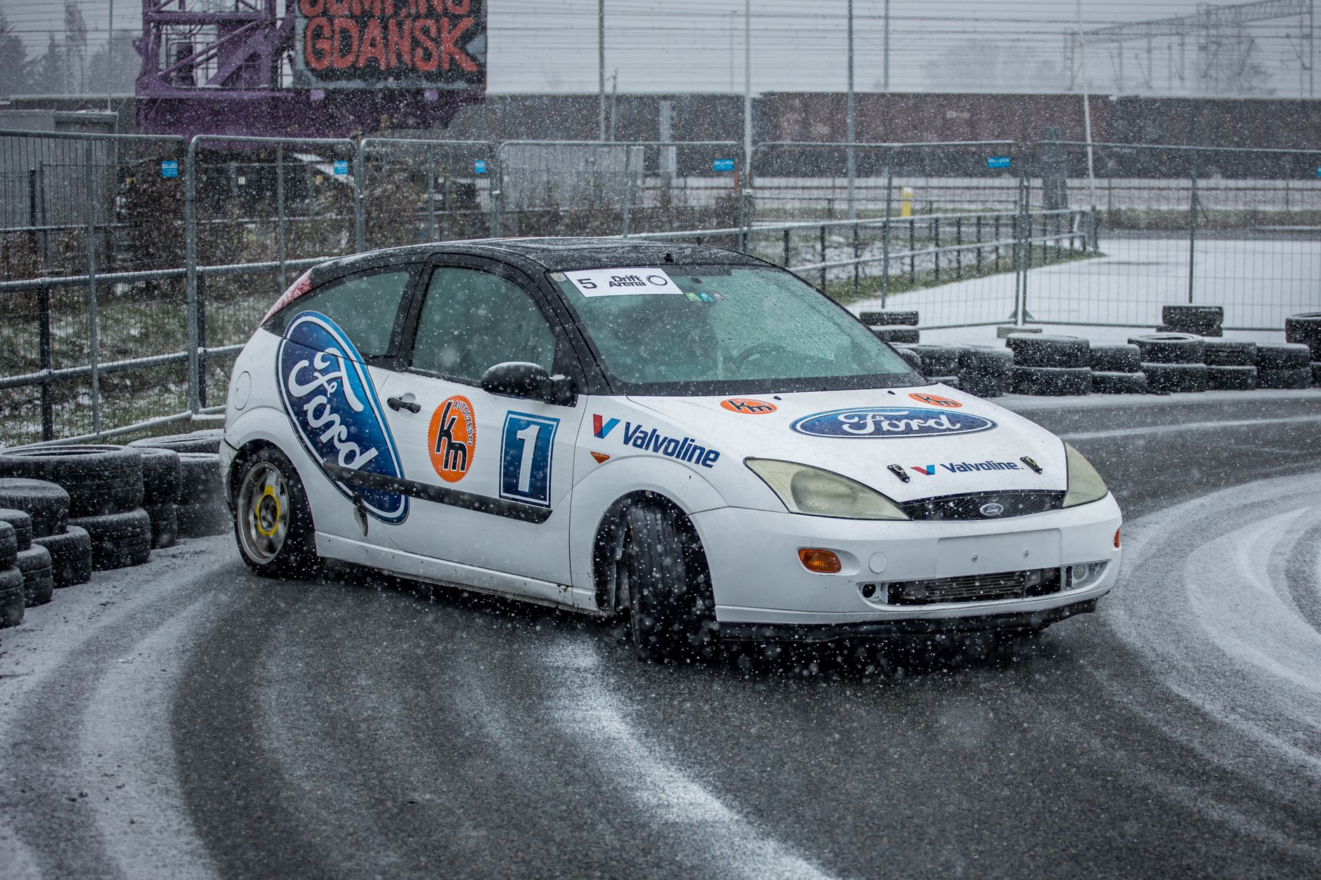 A Ford car drifts on a snowy racetrack in Gdańsk, showcasing motorsport excitement.