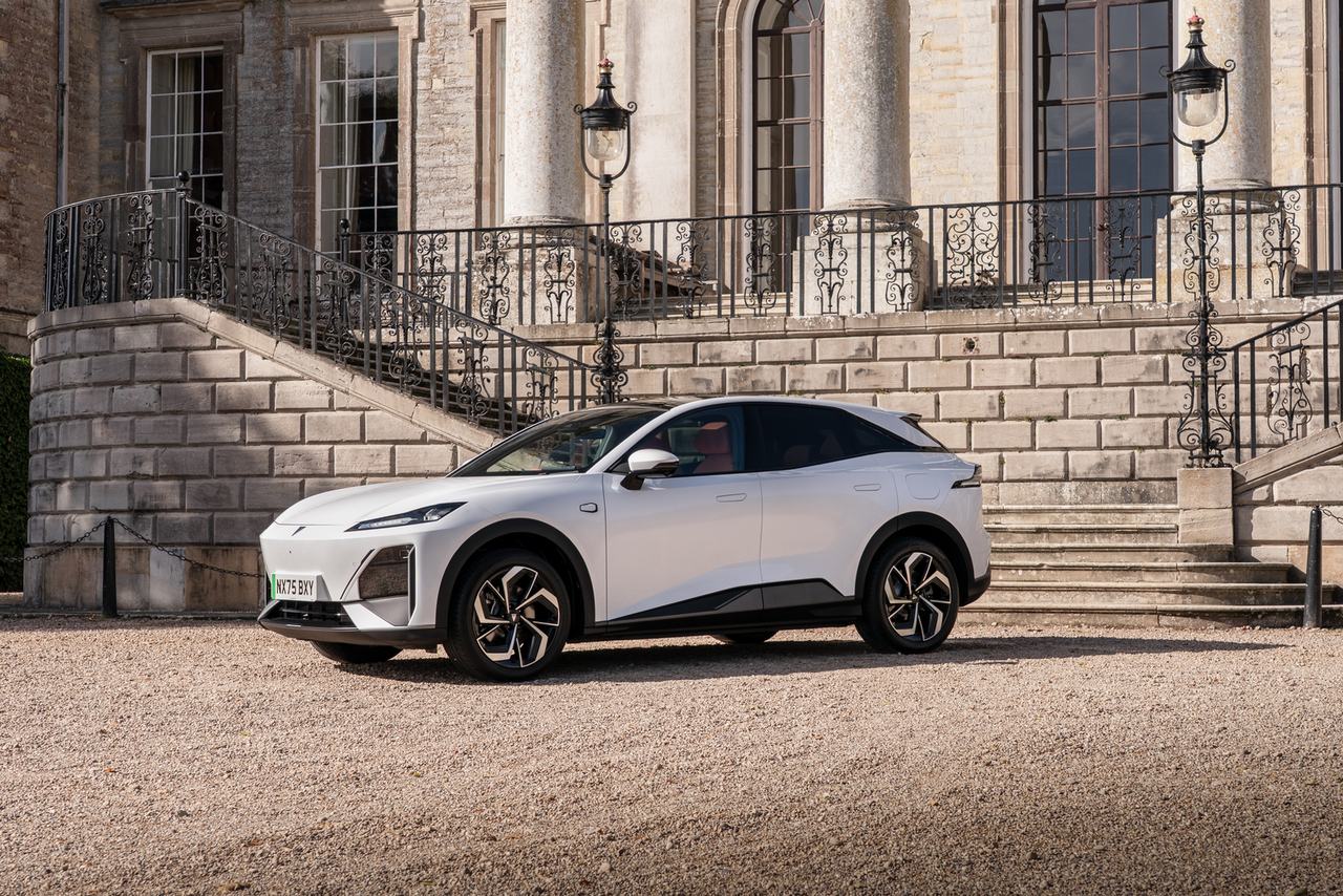 Biały elektryczny SUV zaparkowany przed zabytkową rezydencją z kamiennymi schodami i ozdobnymi balustradami.