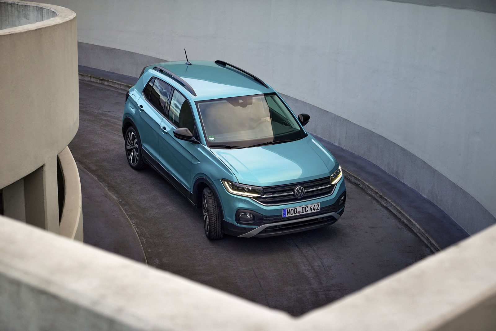 Turkusowy Volkswagen T-Cross jadący po spiralnym podjeździe parkingowym.