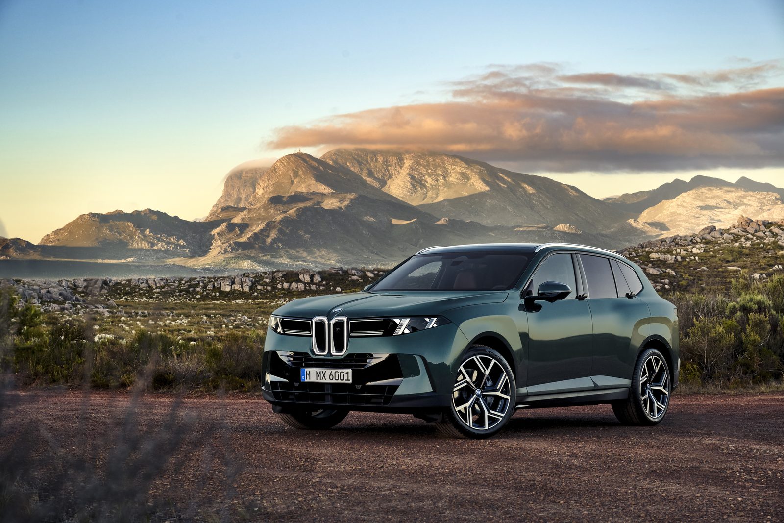 Zielone BMW X5 zaparkowane na tle górskiego krajobrazu o zachodzie słońca.