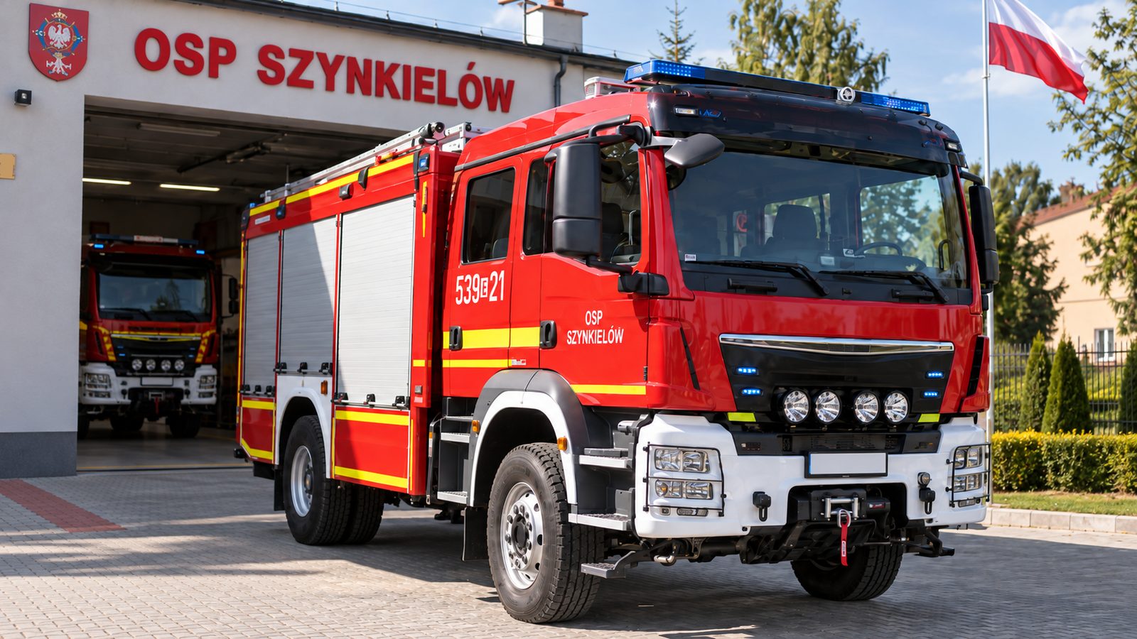 Nowoczesny samochód ratowniczo-gaśniczy OSP Szynkielów przed remizą strażacką z polską flagą.