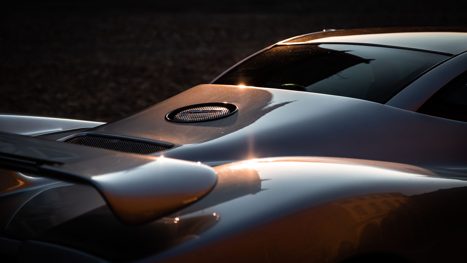 Close-up of a sleek supercar's aerodynamic design with sunlit reflections highlighting its curves.