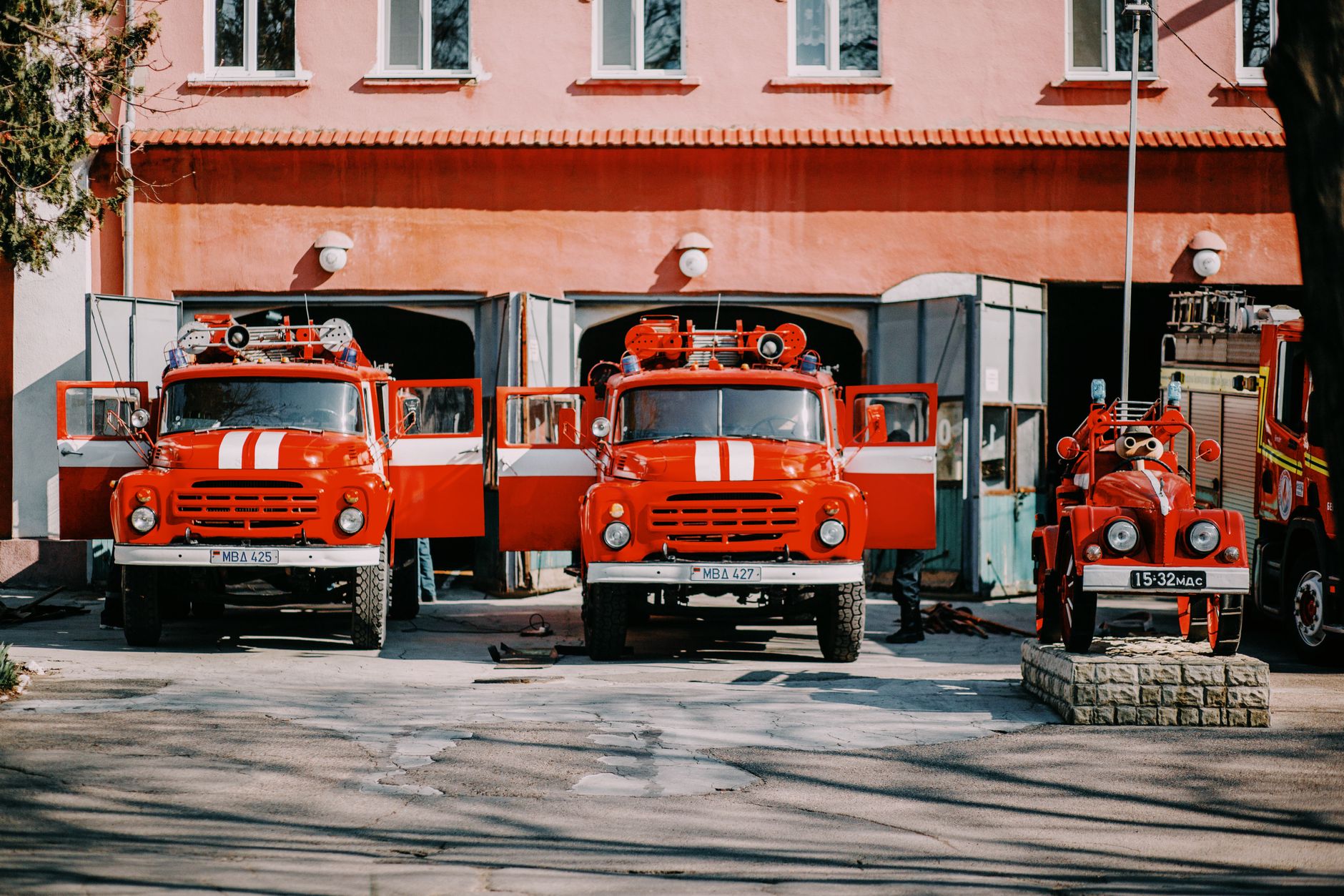 Front view of vintage red fire trucks parked side by side at a fire station outdoors.