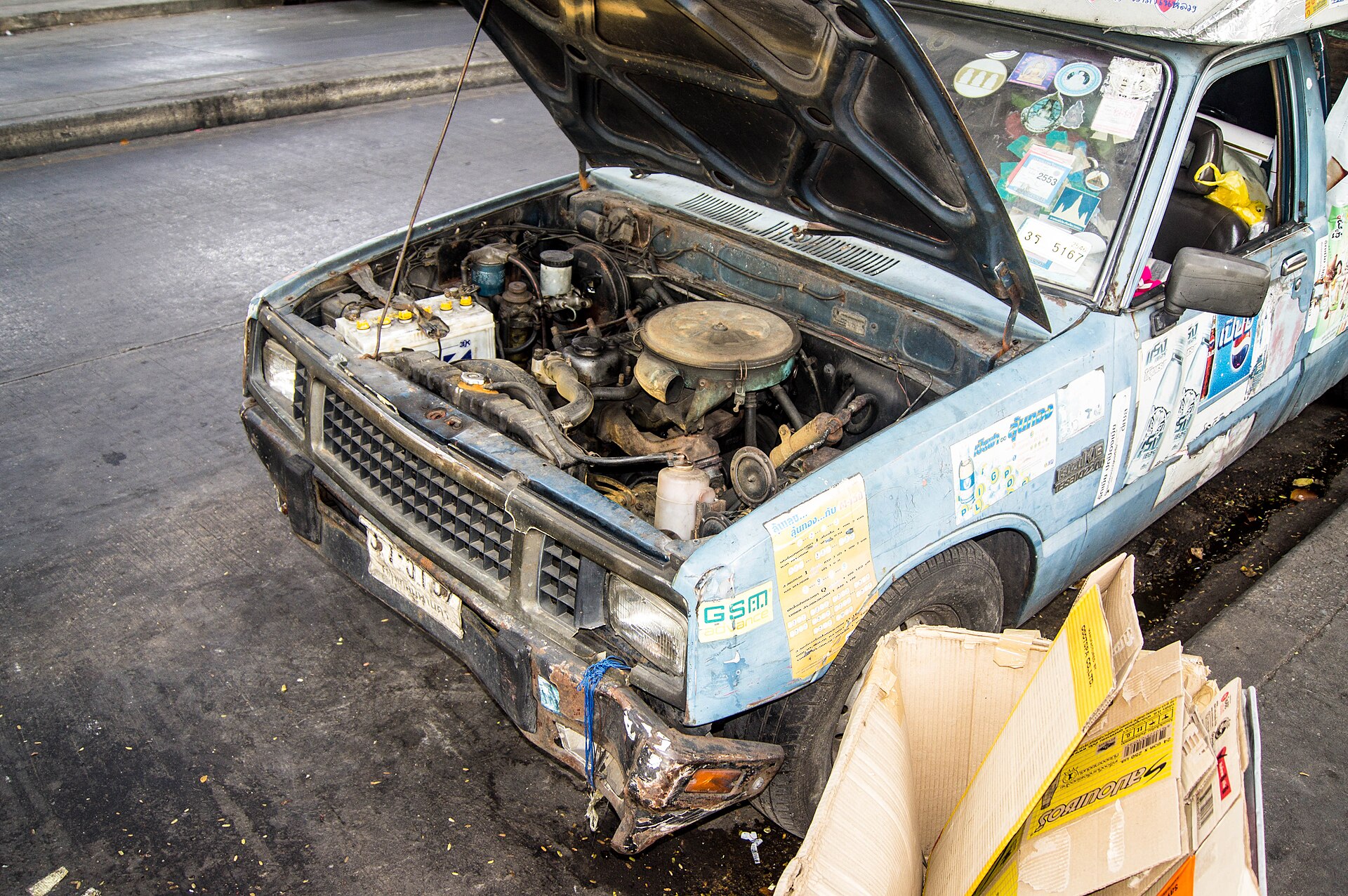 Isuzu KB 2200 Diesel with hood up in Bangkok, extensive assortment of faded stickers on body and windshield