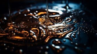 Makrofotografia lejącego się oleju na ciemnym tle z refleksami światła i detalami kropli.