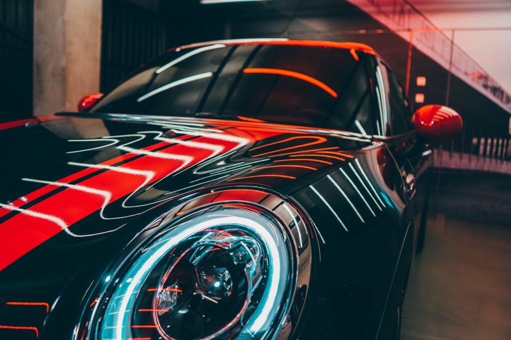 Close-up of a black sports car with vibrant red and white neon light reflections, parked in an urban garage.